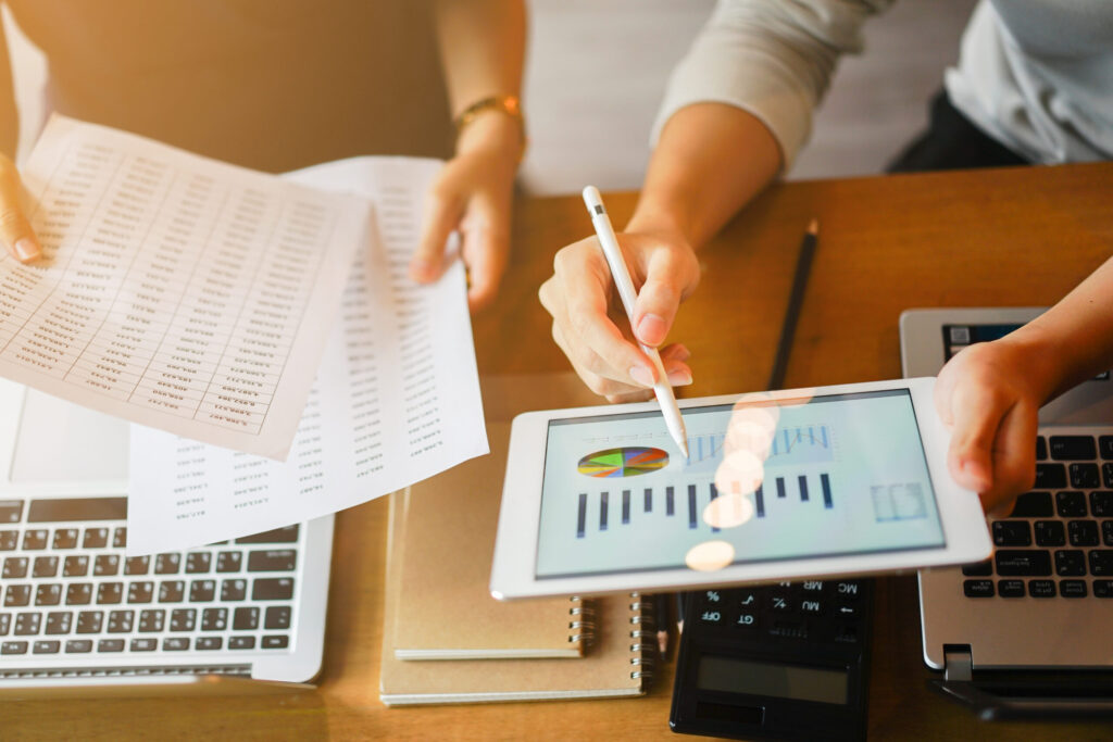 close up group of businessman use stylus pen for explaining dashboard about company's profit monthly on tablet and businesswoman holding report paper for collaborate work at meeting event , business finance concept