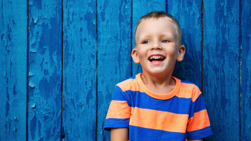 Portrait of happy joyful beautiful little boy against the old textured blue wall.