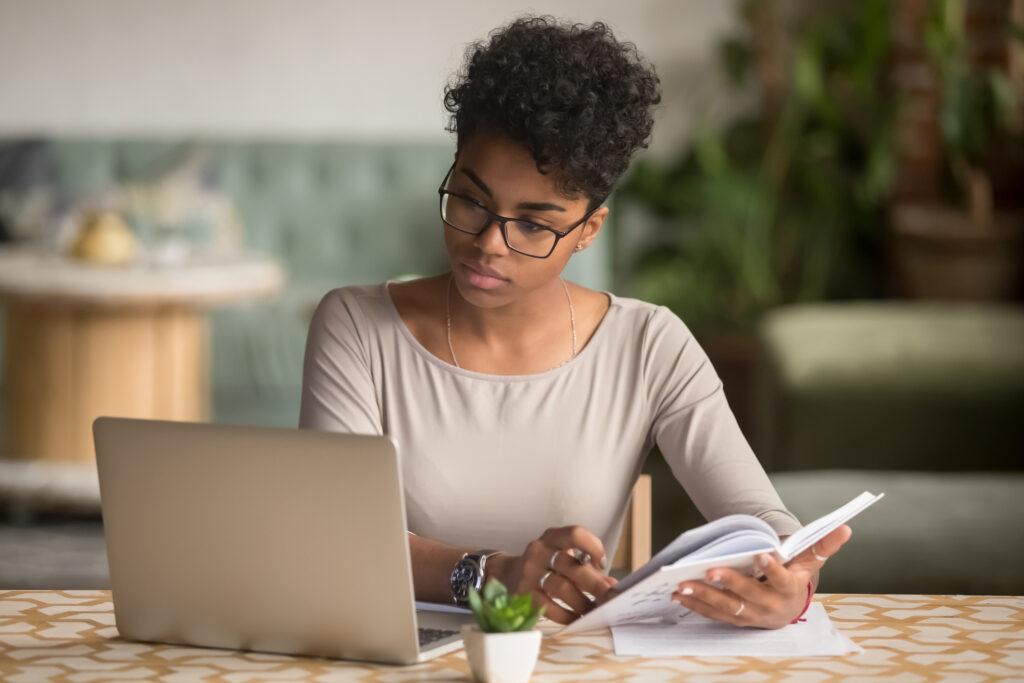 A woman holding a book and reading from a laptop and book.