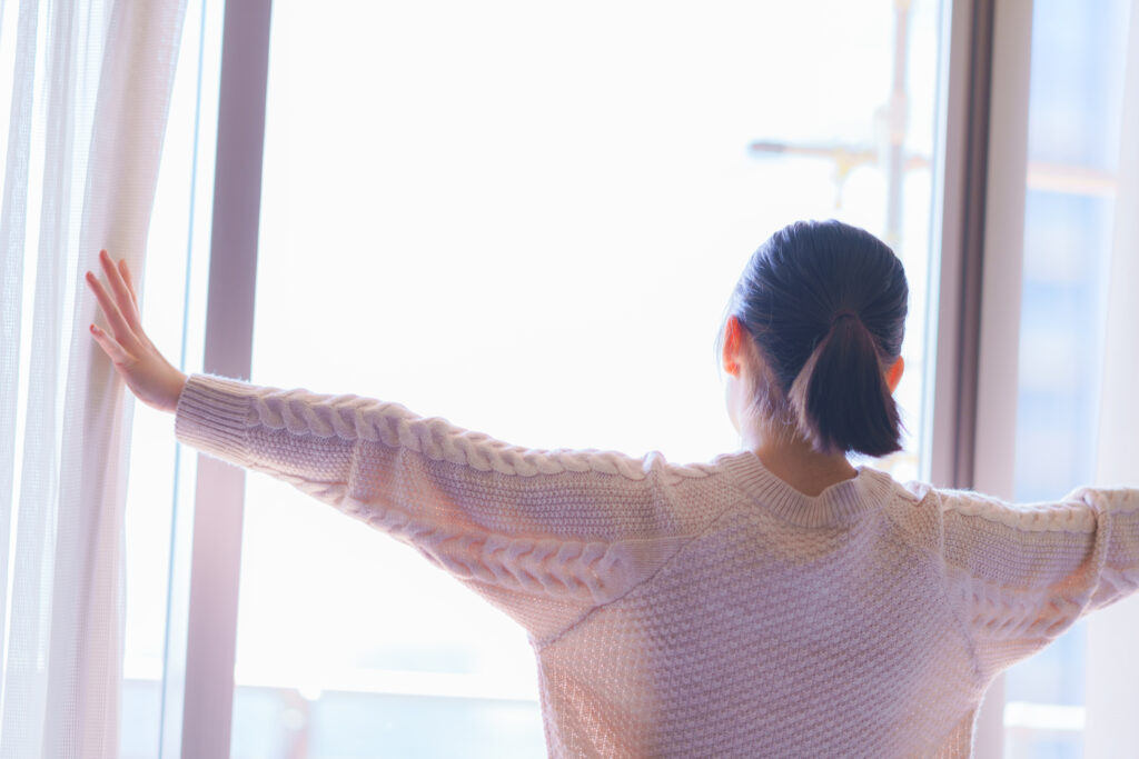 A woman opening curtains, bright day.