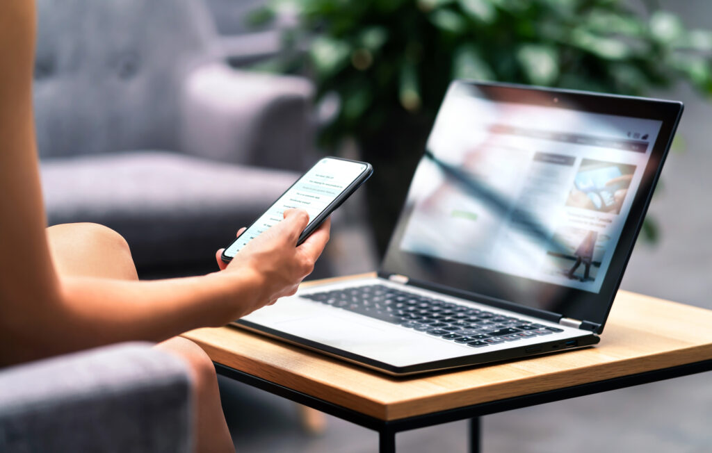 A person using phone and laptop to browse different sites. 